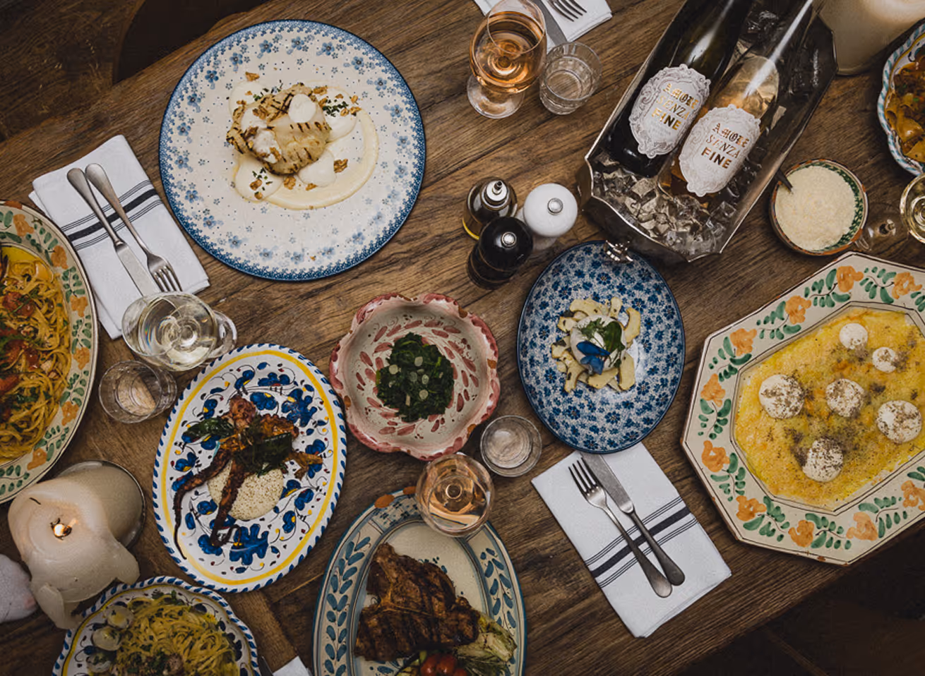 Italienische Tavolata mit vielfältigen Gerichten wie Pasta, gegrilltem Fisch, Fleisch und Antipasti auf bunten Keramiktellern – stilvoll angerichtet auf rustikalem Holztisch im GIGI Restaurant.