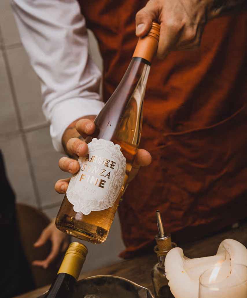 Nahaufnahme einer Hand, die eine Flasche Roséwein mit dem Etikett ‚Amore Senza Fine' hält – stilvolle Getränkeszene im GIGI Restaurant.